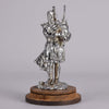 Bagpipes Car Bonet Mascot in the form of a Scotsman dressed in a kilt playing the bagpipes. Exhibiting a well polished surface and fine hand finished detail it is raised and fitted on a stepped circular stand