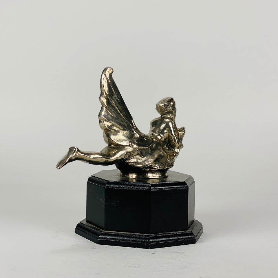 Wave rider Car bonnet mascot by Georges Delperier  in the form of a winged woman laying on her front in a casual pose riding on top of a wave, with very fine hand finished detail. Raised on an octagonal wooden plinth