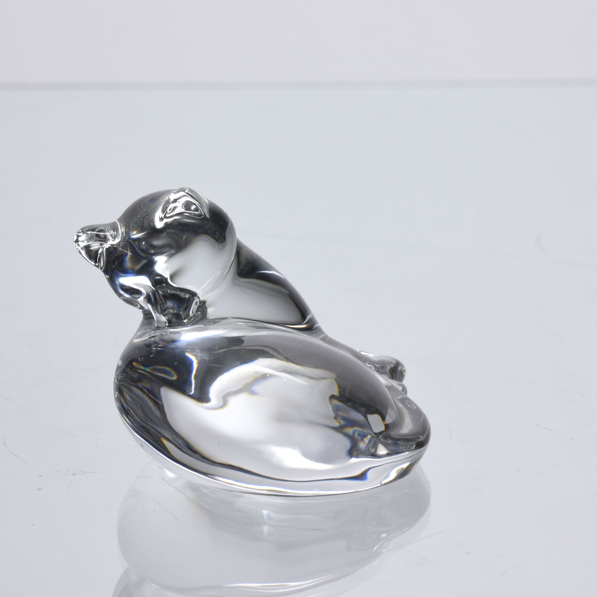 A charming mid 20th Century clear glass study of a relaxed cat in a reclining position grooming itself, with excellent smooth tactile surface, signed under base 