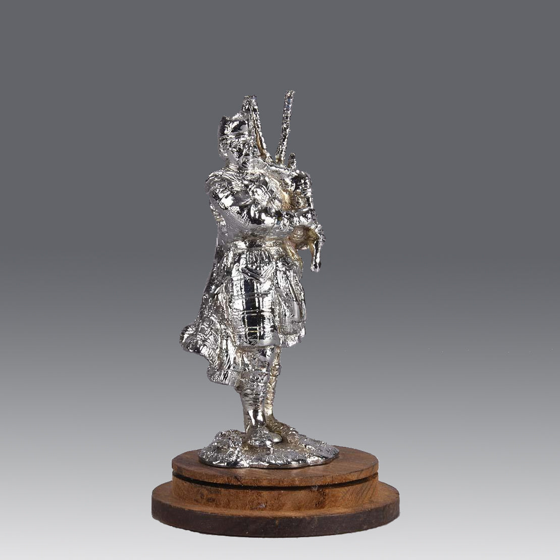 Bagpipes Car Bonet Mascot in the form of a Scotsman dressed in a kilt playing the bagpipes. Exhibiting a well polished surface and fine hand finished detail it is raised and fitted on a stepped circular stand