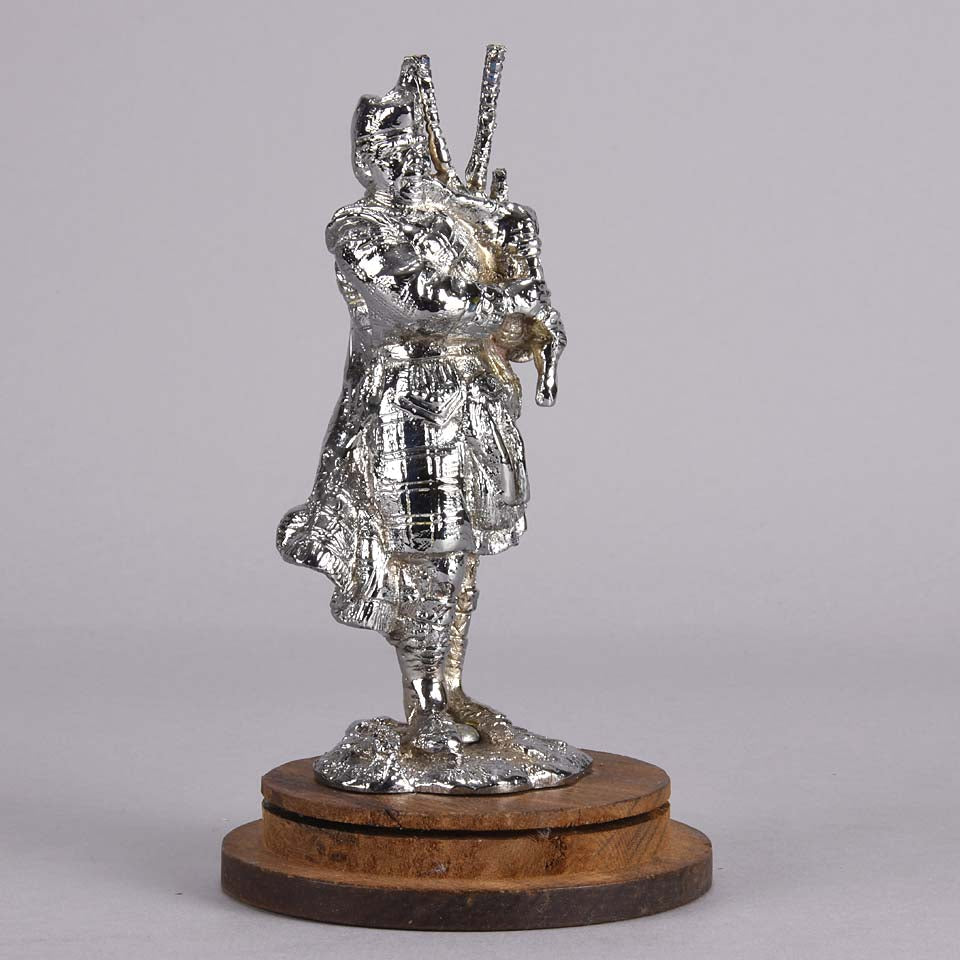 Bagpipes Car Bonet Mascot in the form of a Scotsman dressed in a kilt playing the bagpipes. Exhibiting a well polished surface and fine hand finished detail it is raised and fitted on a stepped circular stand