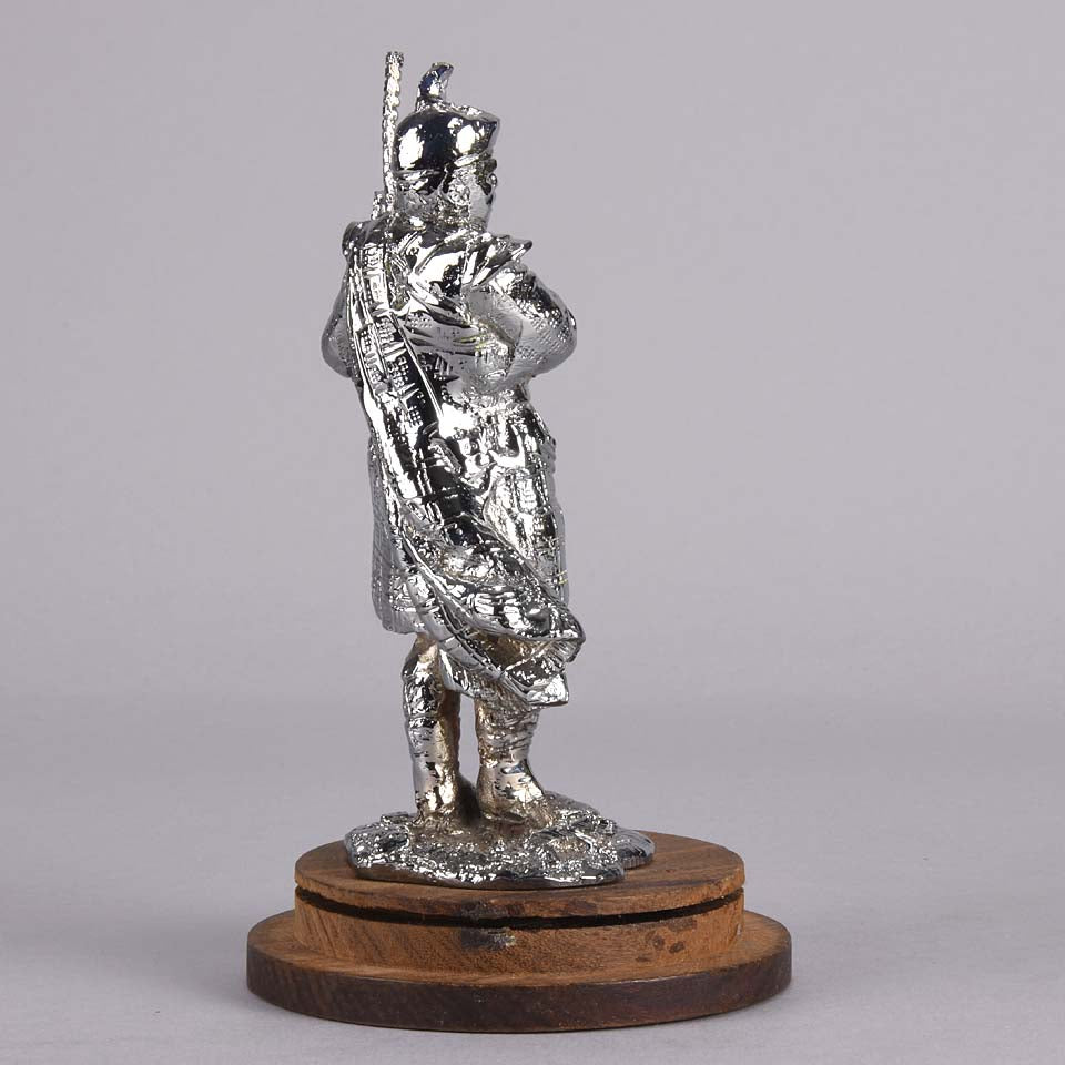 Bagpipes Car Bonet Mascot in the form of a Scotsman dressed in a kilt playing the bagpipes. Exhibiting a well polished surface and fine hand finished detail it is raised and fitted on a stepped circular stand