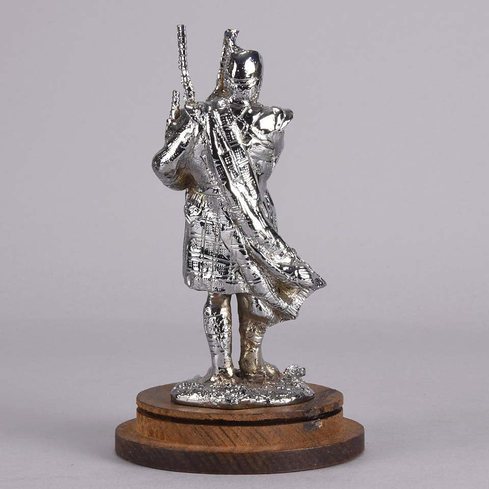 Bagpipes Car Bonet Mascot in the form of a Scotsman dressed in a kilt playing the bagpipes. Exhibiting a well polished surface and fine hand finished detail it is raised and fitted on a stepped circular stand