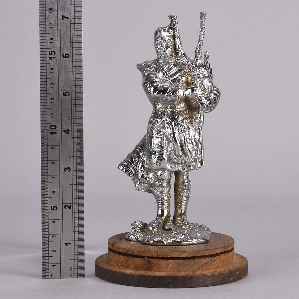 Bagpipes Car Bonet Mascot in the form of a Scotsman dressed in a kilt playing the bagpipes. Exhibiting a well polished surface and fine hand finished detail it is raised and fitted on a stepped circular stand