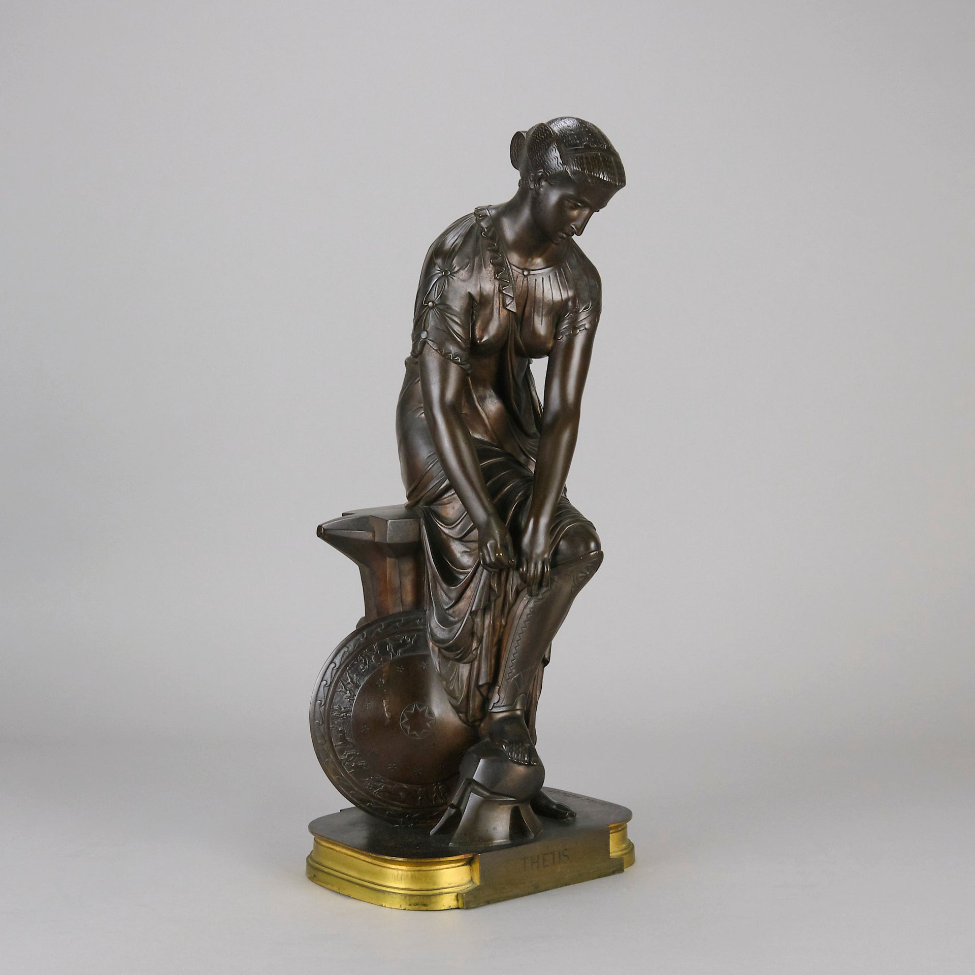 Thetis by Emile Hébert - a French late 19th Century bronze, of a striking female warrior figure known as Thetis the Greek Goddess of War. She is adjusting her shin guards in preparation for her next opponent, whilst sitting on an anvil. Raised on top of a partly gilded base