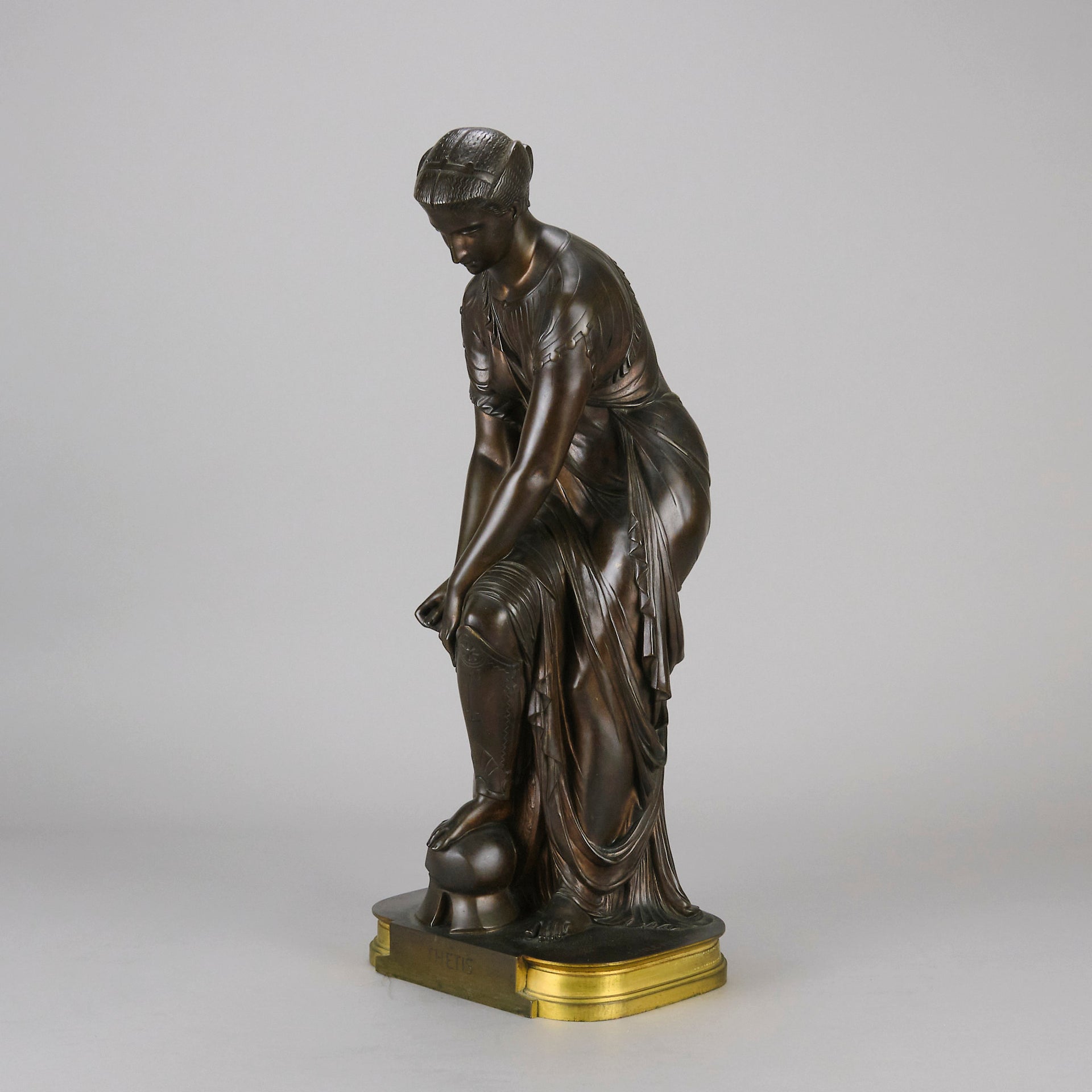 Thetis by Emile Hébert - a French late 19th Century bronze, of a striking female warrior figure known as Thetis the Greek Goddess of War. She is adjusting her shin guards in preparation for her next opponent, whilst sitting on an anvil. Raised on top of a partly gilded base