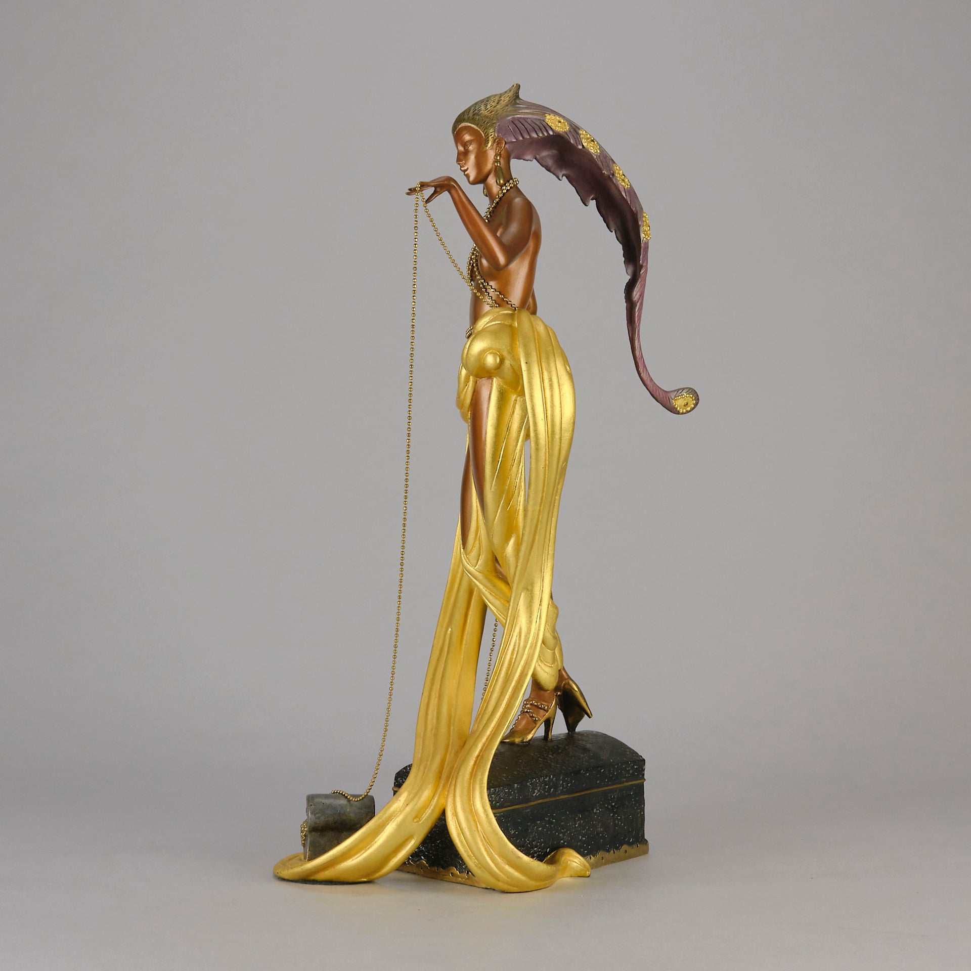 Pleasures of the Courtesan by Erté an attractive limited edition 20th Century bronze figure modelled as a beautiful young woman holding a long golden chain from a treasure chest at her feet wearing only an flamboyant skirt & headdress