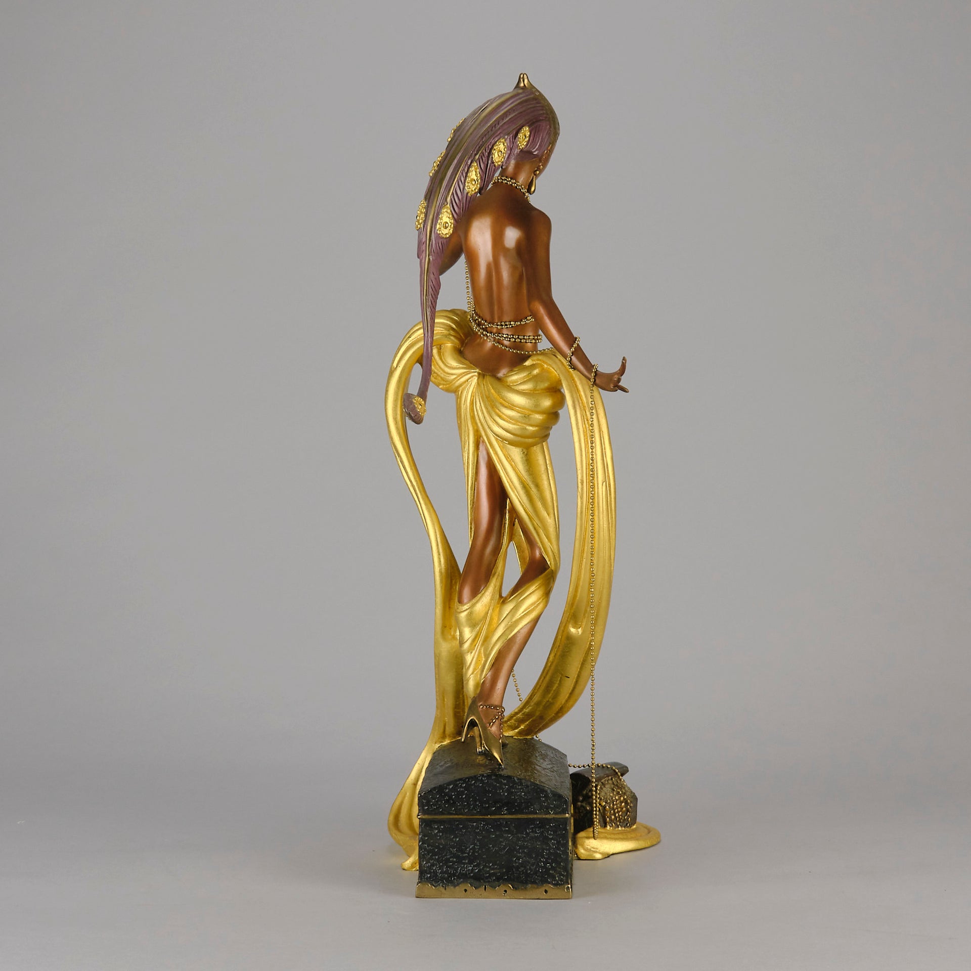 Pleasures of the Courtesan by Erté an attractive limited edition 20th Century bronze figure modelled as a beautiful young woman holding a long golden chain from a treasure chest at her feet wearing only an flamboyant skirt & headdress