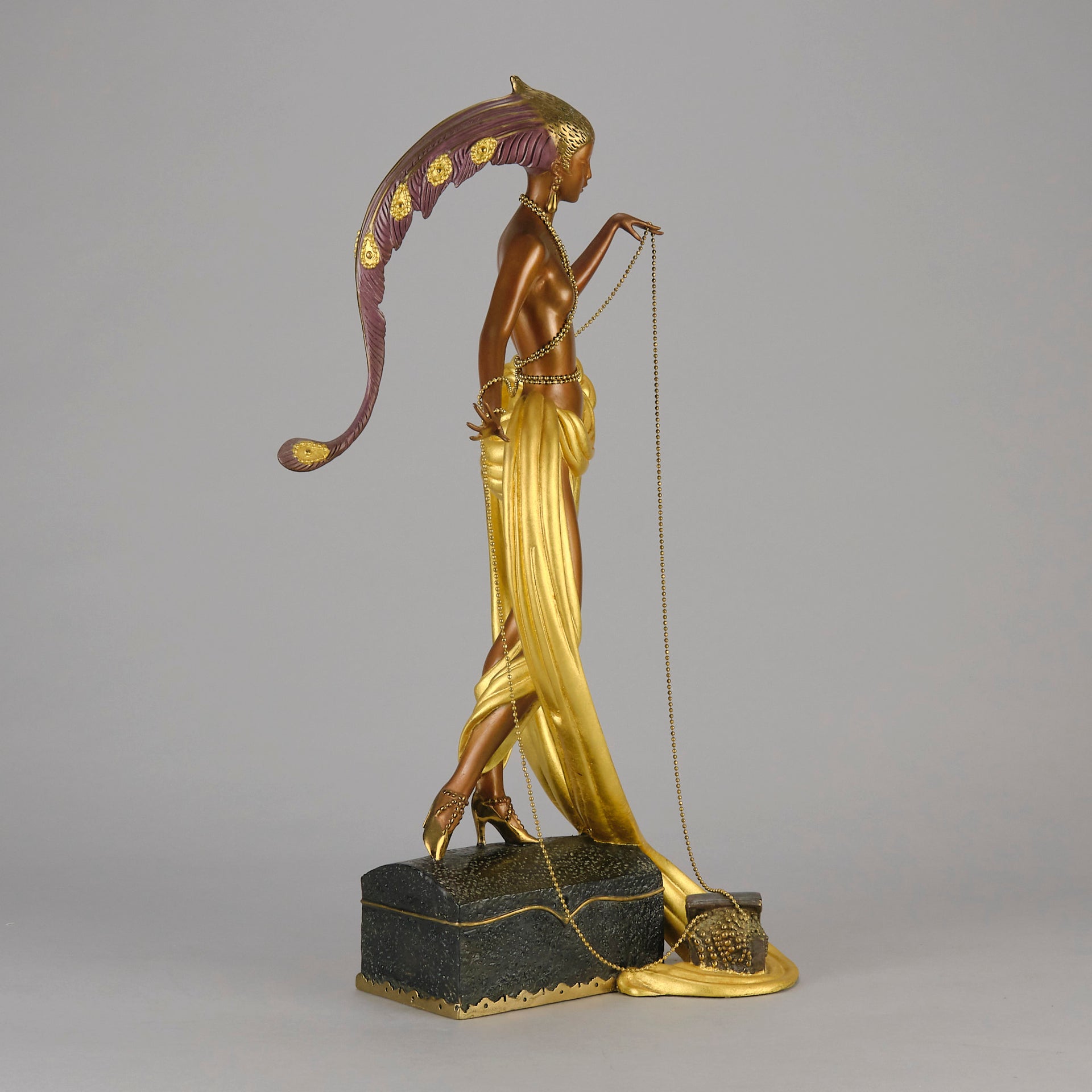 Pleasures of the Courtesan by Erté an attractive limited edition 20th Century bronze figure modelled as a beautiful young woman holding a long golden chain from a treasure chest at her feet wearing only an flamboyant skirt & headdress