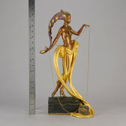 Pleasures of the Courtesan by Erté an attractive limited edition 20th Century bronze figure modelled as a beautiful young woman holding a long golden chain from a treasure chest at her feet wearing only an flamboyant skirt & headdress