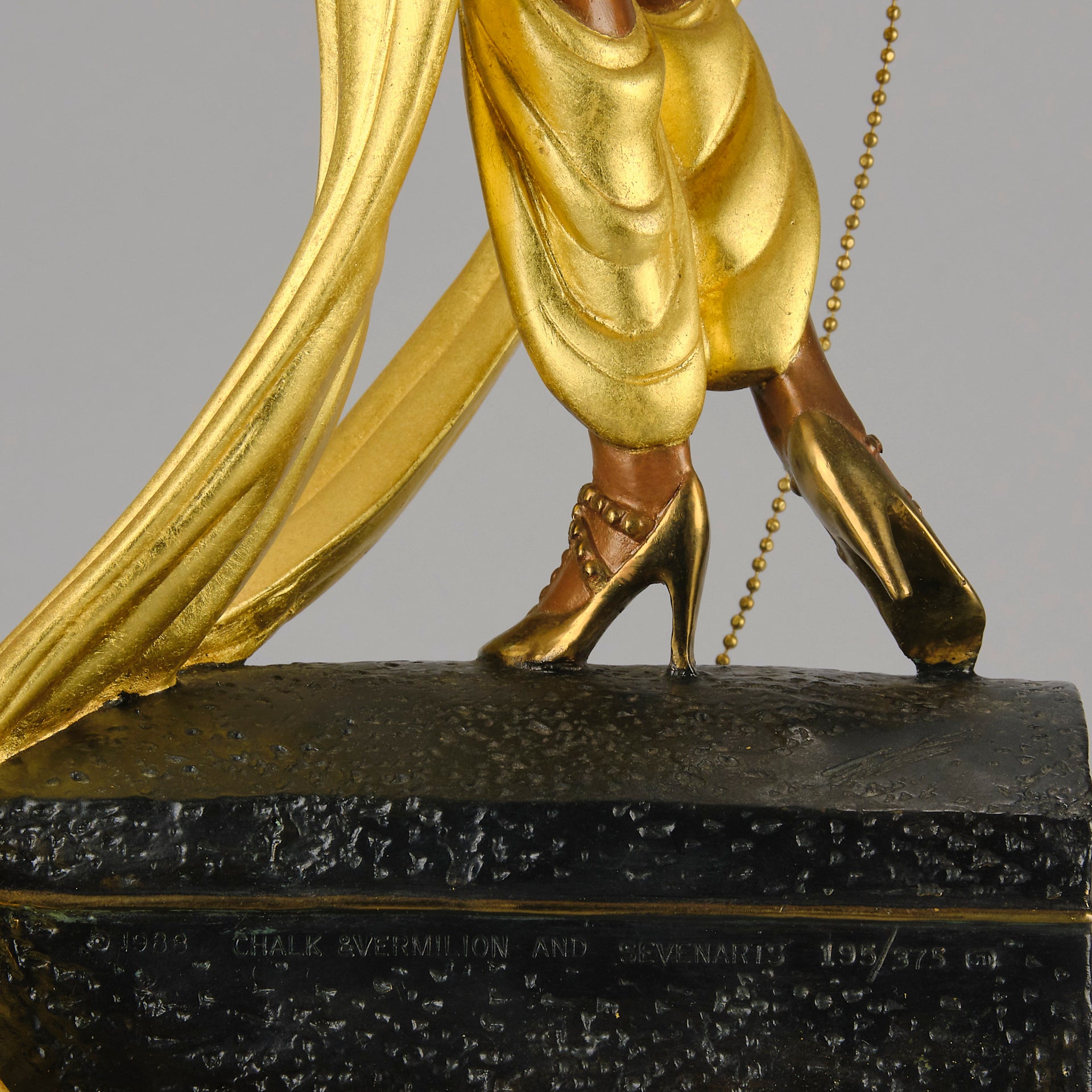 Pleasures of the Courtesan by Erté an attractive limited edition 20th Century bronze figure modelled as a beautiful young woman holding a long golden chain from a treasure chest at her feet wearing only an flamboyant skirt & headdress