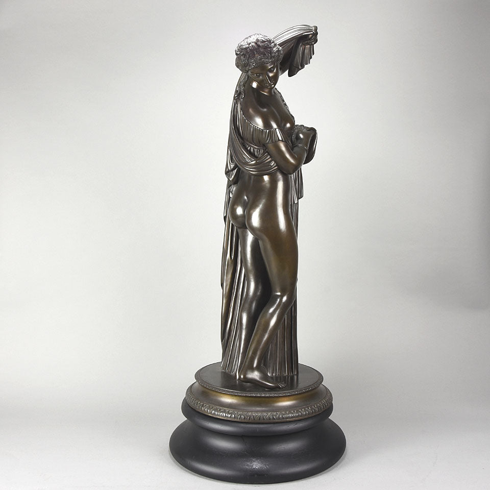 Callipygian Venus an Antique Bronze Figure depicting a partially draped woman, raising her light peplos (draped clothing) to uncover her hips and buttocks, and looking back and down over her shoulder