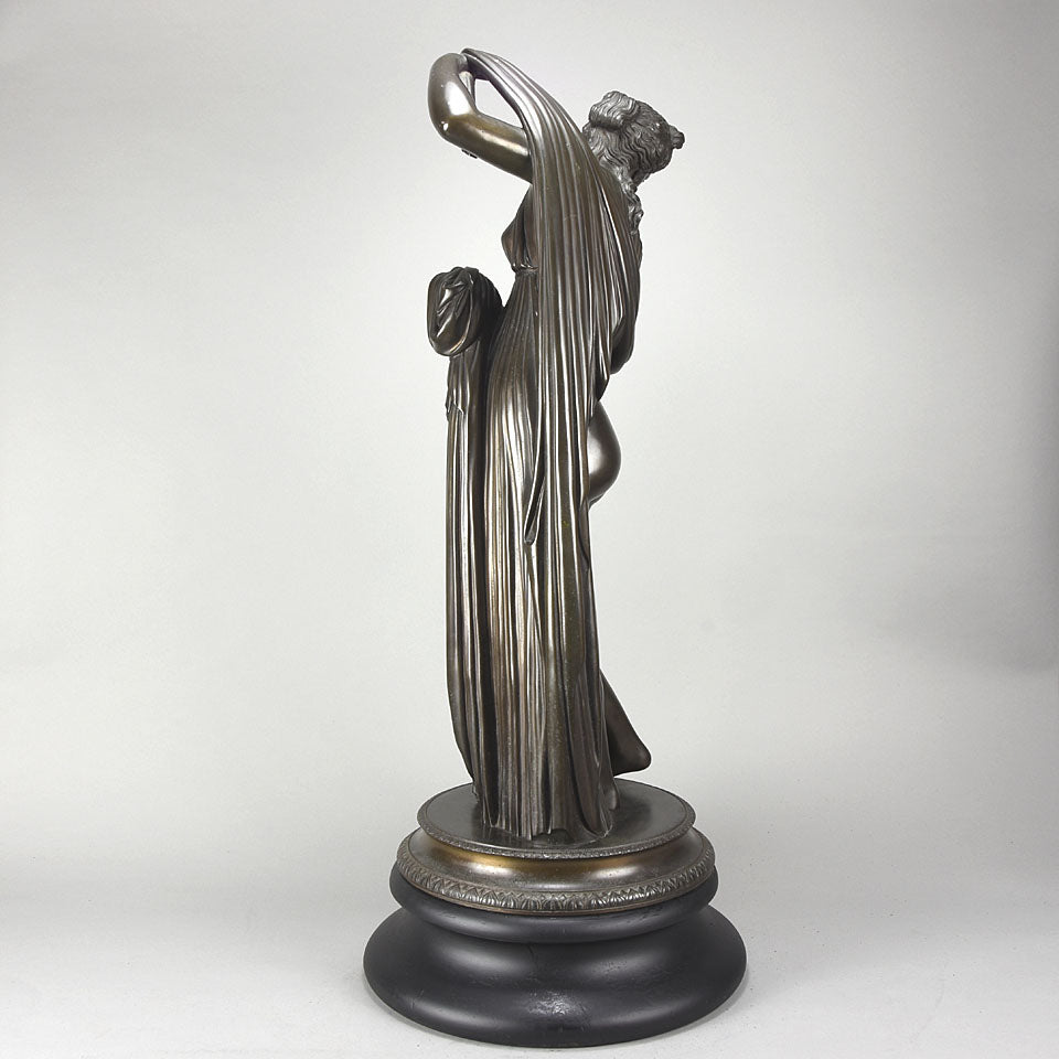 Callipygian Venus an Antique Bronze Figure depicting a partially draped woman, raising her light peplos (draped clothing) to uncover her hips and buttocks, and looking back and down over her shoulder