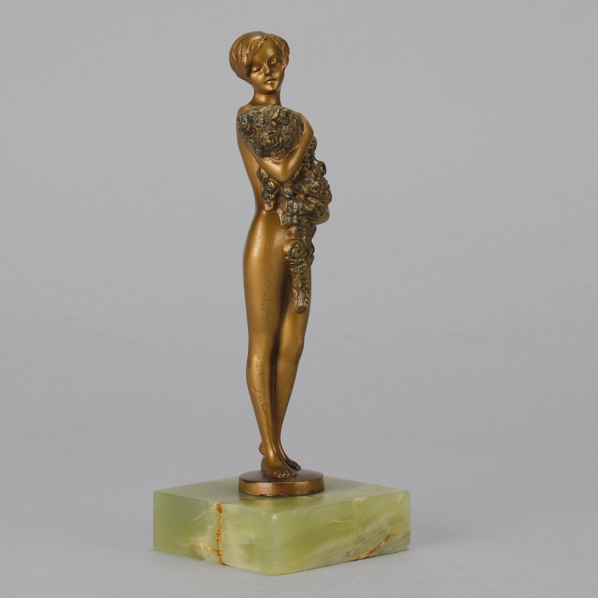 The Bouquet by Joseph Lorenzl an elegant early 20th Century Art Deco cold painted bronze figure of a young beauty holding a large bouquet of flowers covering her modesty raised on a green onyx base 