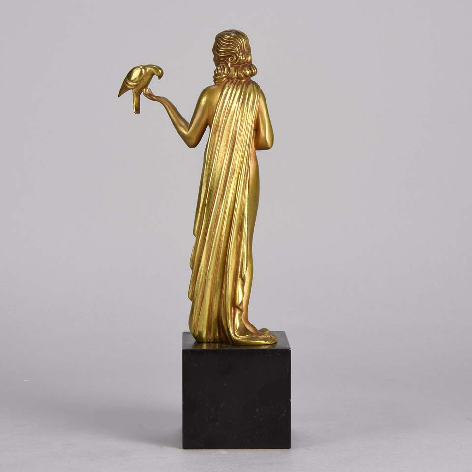 Femme avec Oiseau by Pierre Laurel an antique bronze figure of a semi clad young woman holding a bird in classic high Art Deco pose with excellent gilt patination and intricate surface detail on a square shaped black marble base 