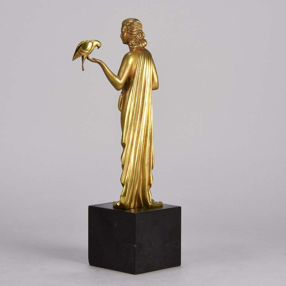 Femme avec Oiseau by Pierre Laurel an antique bronze figure of a semi clad young woman holding a bird in classic high Art Deco pose with excellent gilt patination and intricate surface detail on a square shaped black marble base 
