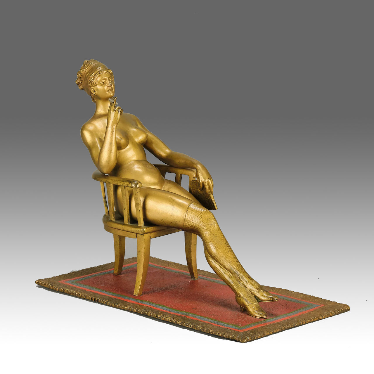 Vienna Bronze Seated Lady - an early 20th Century cold-painted Austrian bronze figure of an attractive lady seated on an arm chair wearing only a pair of stockings and heals, holding a book whilst enjoying a cigarette