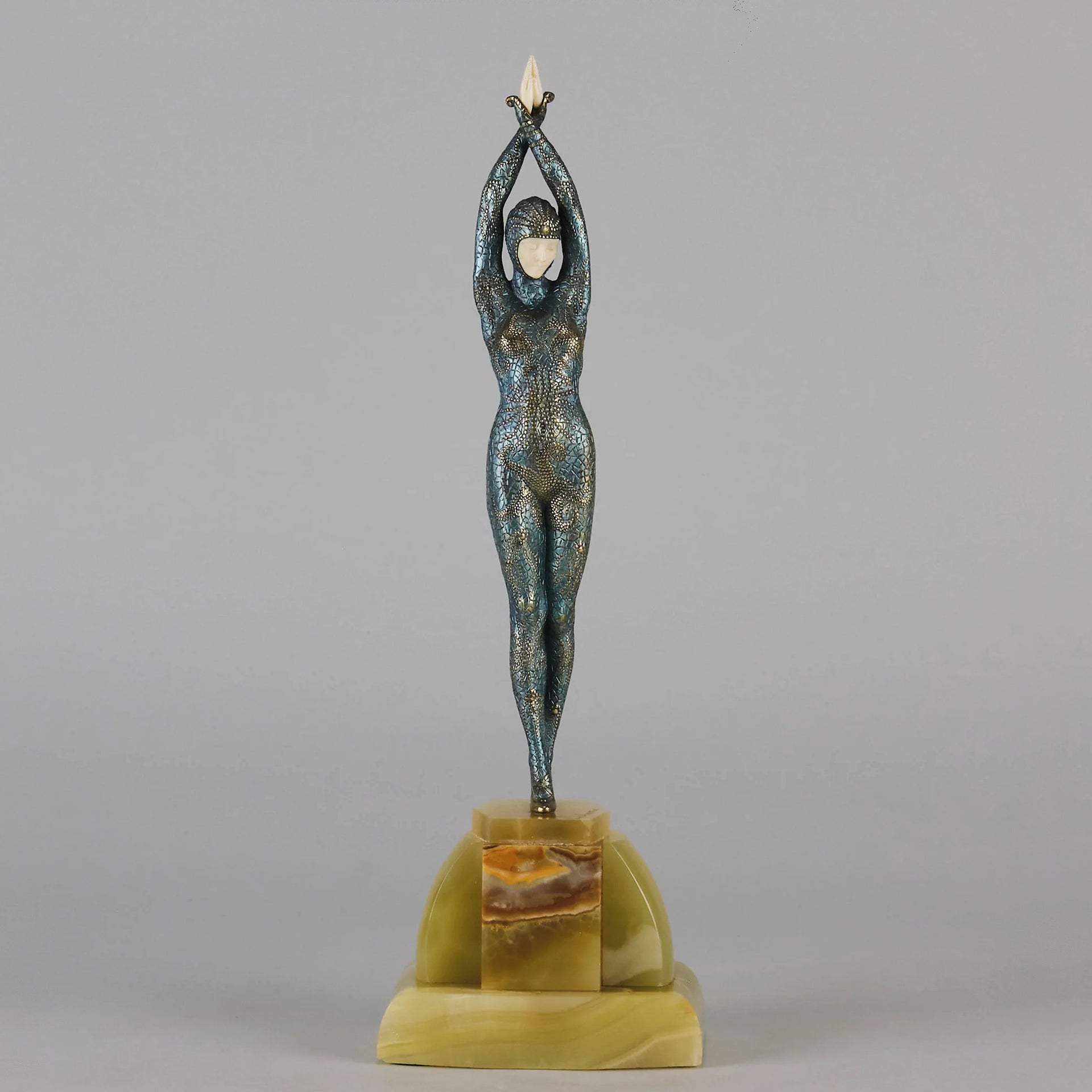  Starfish by Demetre Chiparus a  Art Deco cold painted silver and enamel bronze sculpture with ivory face and hands representing a young female Ballets Russes dancer wearing a metallic blue skin tight leotard further decorated in a bejewelled starfish pattern, modelled reaching upwards with both arms, her hands interlaced. Raised on a shaped onyx base