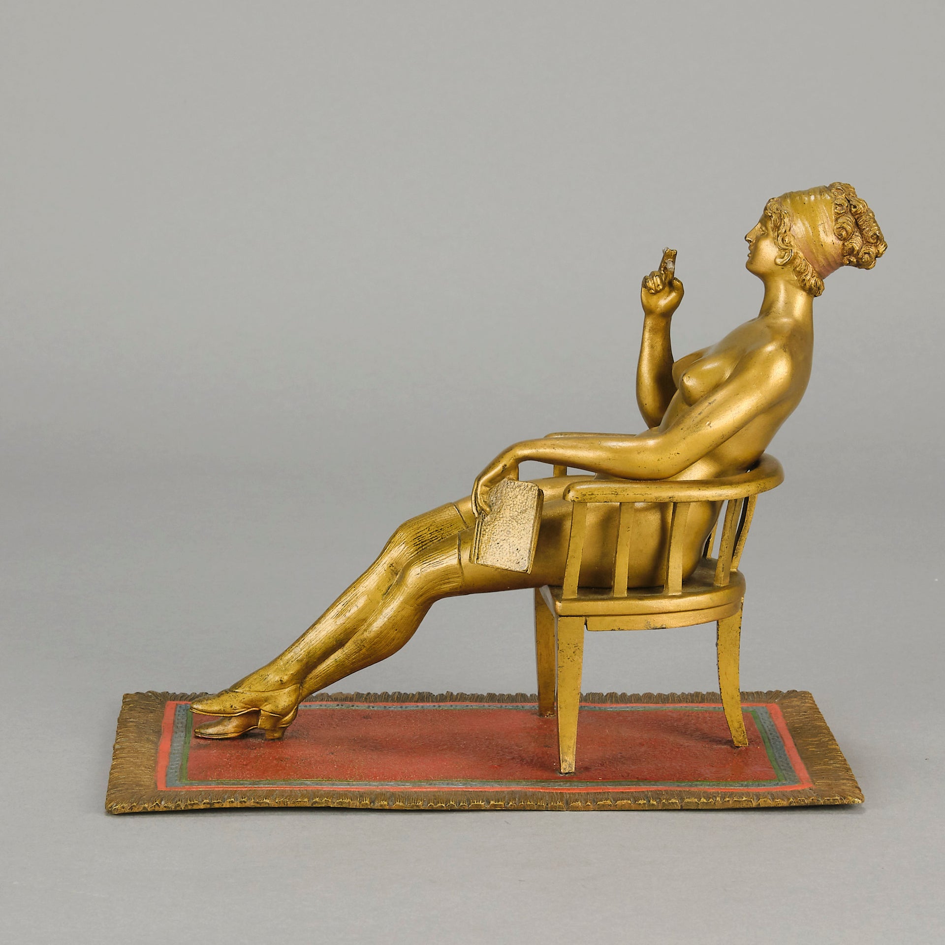 Vienna Bronze Seated Lady - an early 20th Century cold-painted Austrian bronze figure of an attractive lady seated on an arm chair wearing only a pair of stockings and heals, holding a book whilst enjoying a cigarette