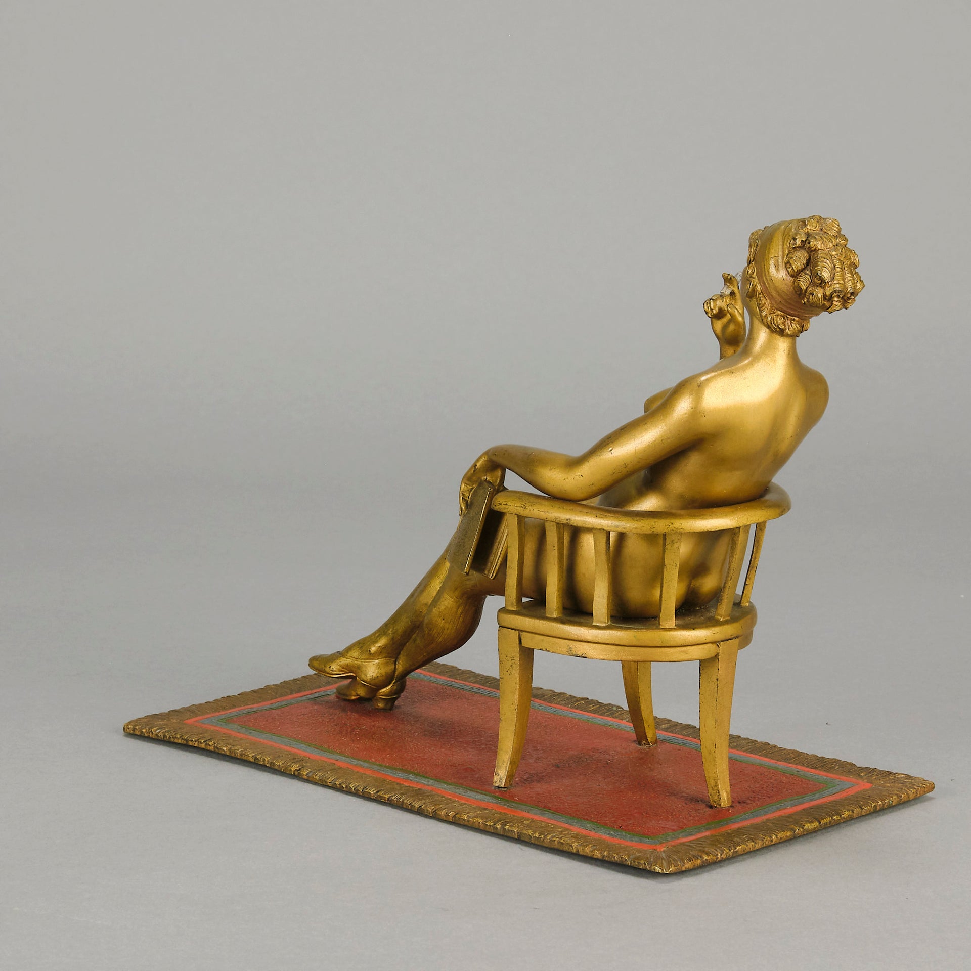 Vienna Bronze Seated Lady - an early 20th Century cold-painted Austrian bronze figure of an attractive lady seated on an arm chair wearing only a pair of stockings and heals, holding a book whilst enjoying a cigarette