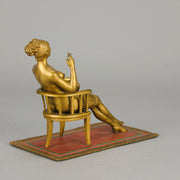 Vienna Bronze Seated Lady - an early 20th Century cold-painted Austrian bronze figure of an attractive lady seated on an arm chair wearing only a pair of stockings and heals, holding a book whilst enjoying a cigarette