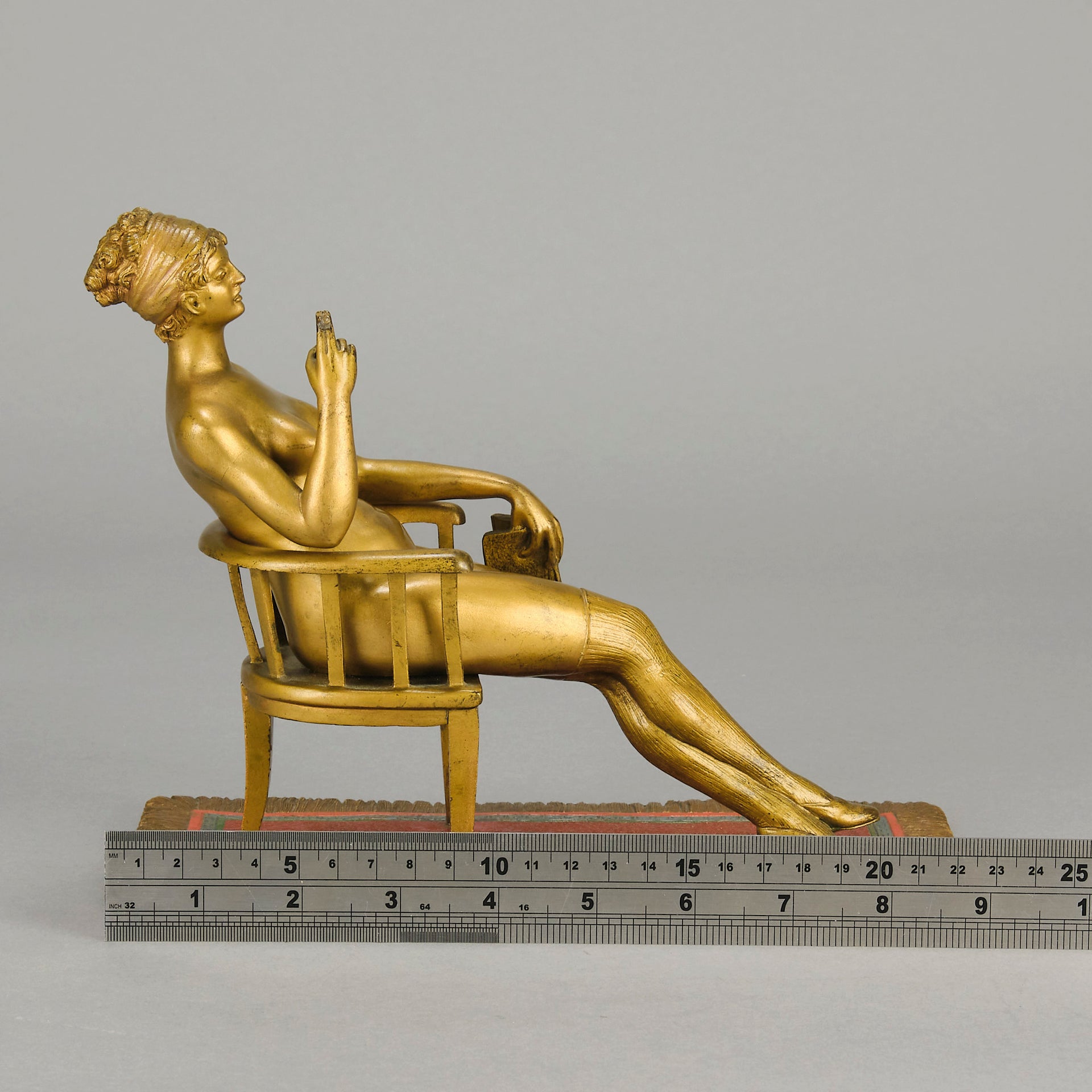 Vienna Bronze Seated Lady - an early 20th Century cold-painted Austrian bronze figure of an attractive lady seated on an arm chair wearing only a pair of stockings and heals, holding a book whilst enjoying a cigarette